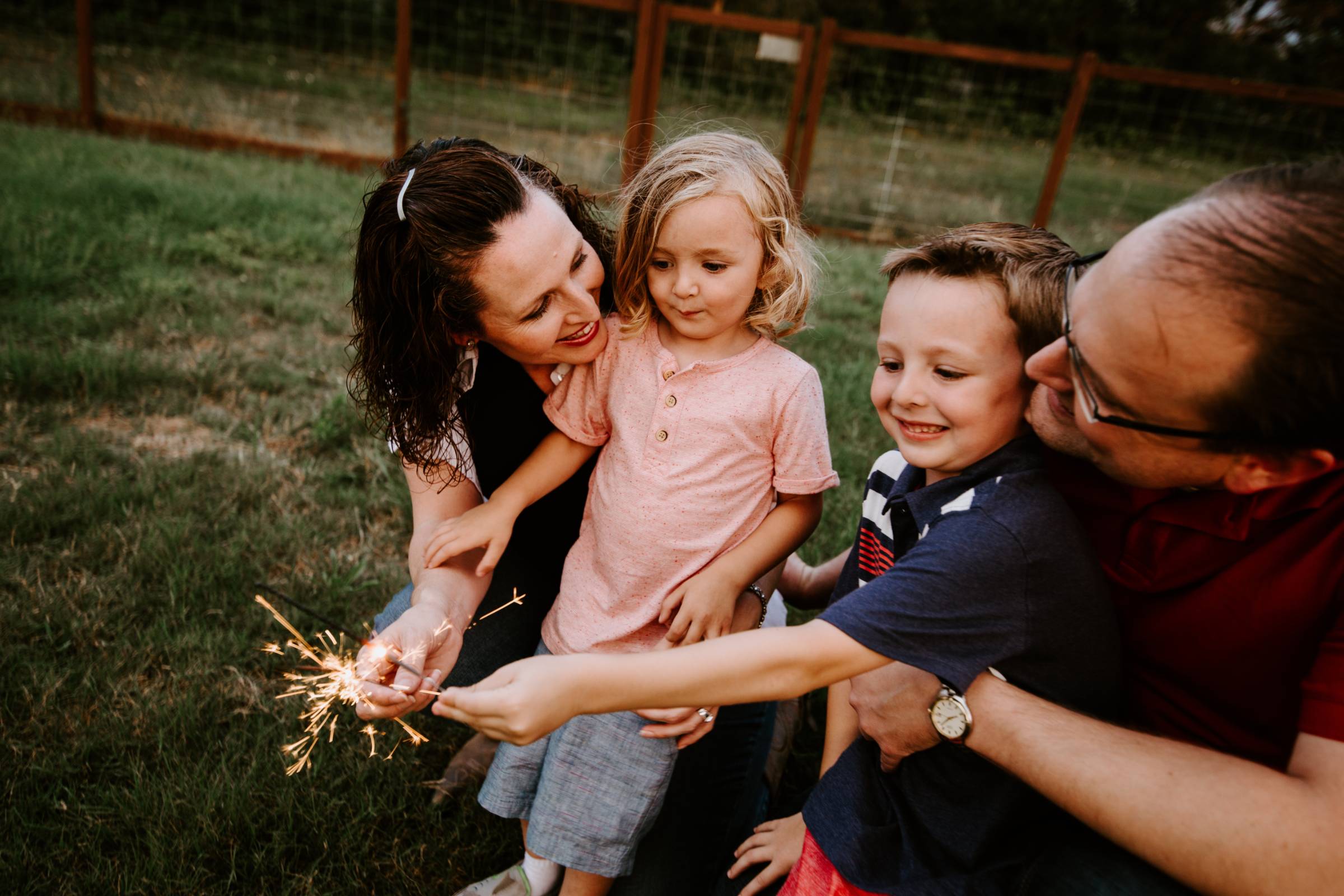 Family of four outside at dusk with parents helping kid hold sparklers