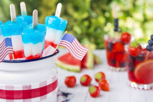fourth of july popsicles on table with small American flags, drinks and fruit in the background