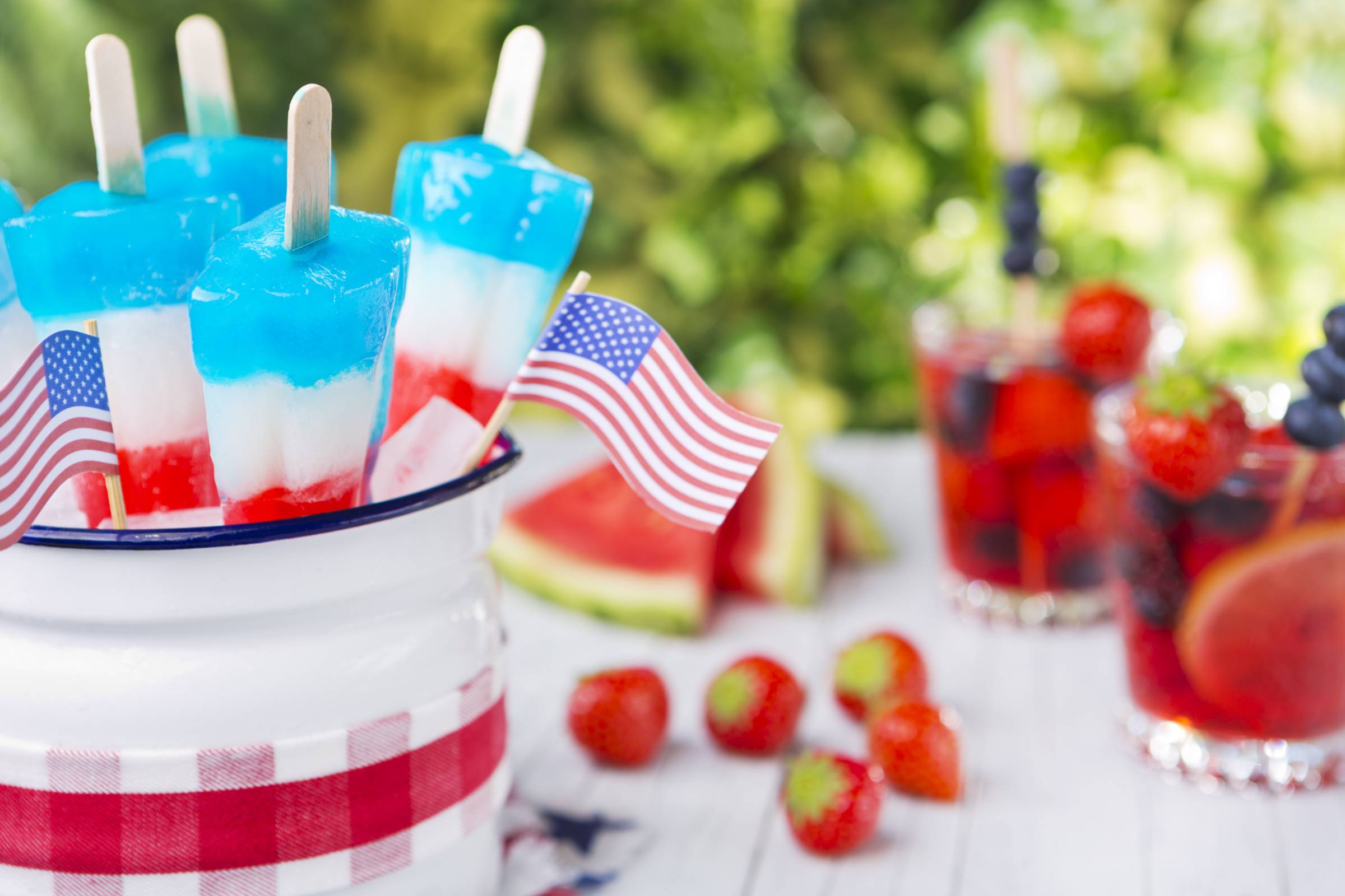 fourth of july popsicles on table with small American flags, drinks and fruit in the background