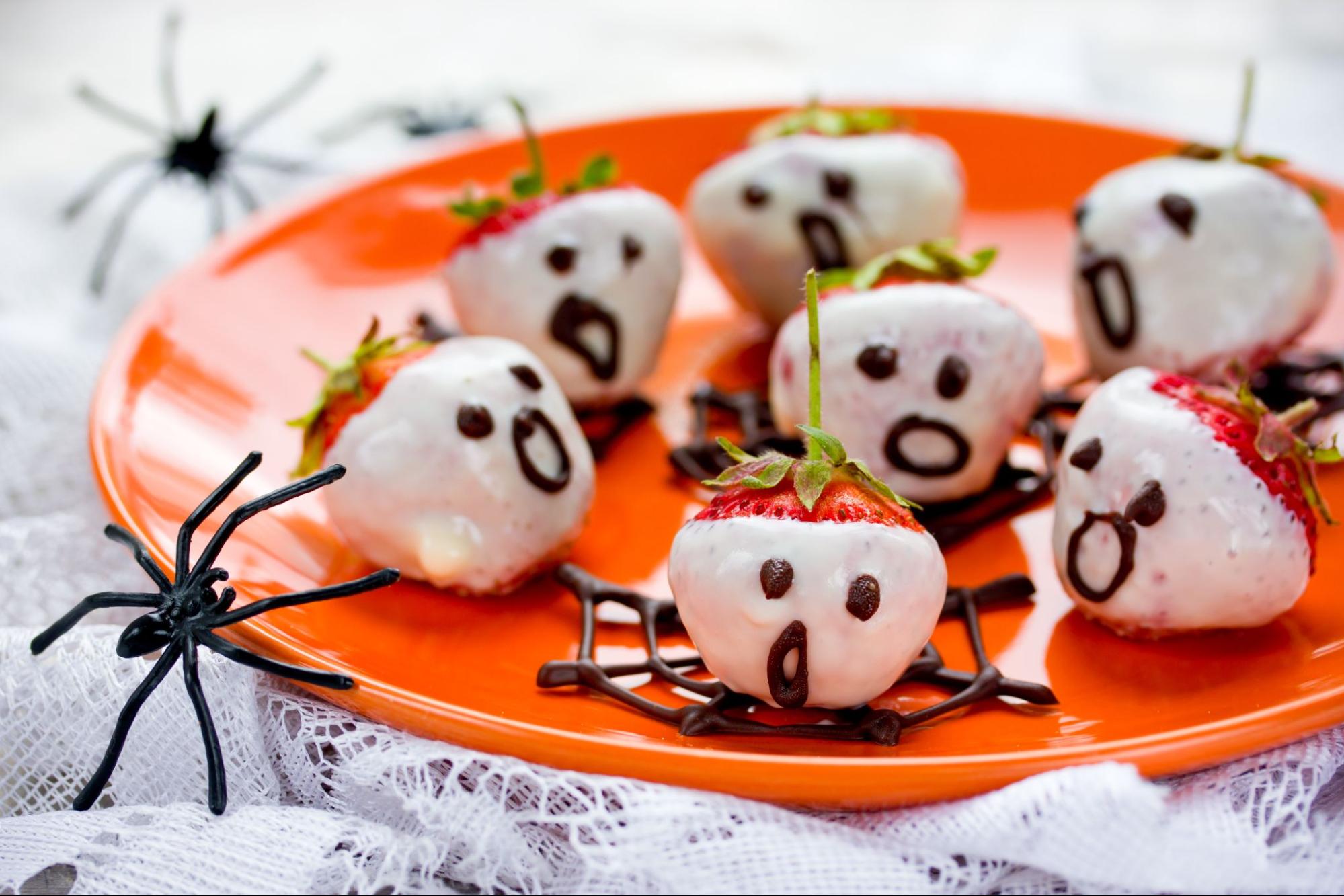 White chocolate-covered strawberries decorated as ghosts on a red plate with Halloween spider decorations ©Anastasia_Panait