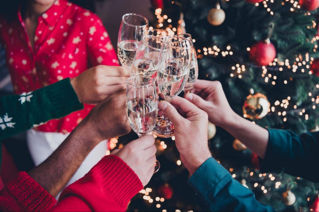 Hands clinking champagne glasses in a cozy Christmas party with a decorated tree in the background ©Roman Samborskyi