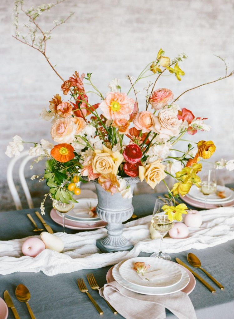 Colorful spring floral centerpiece on dining table with plates and glassware. ©Martha Graham