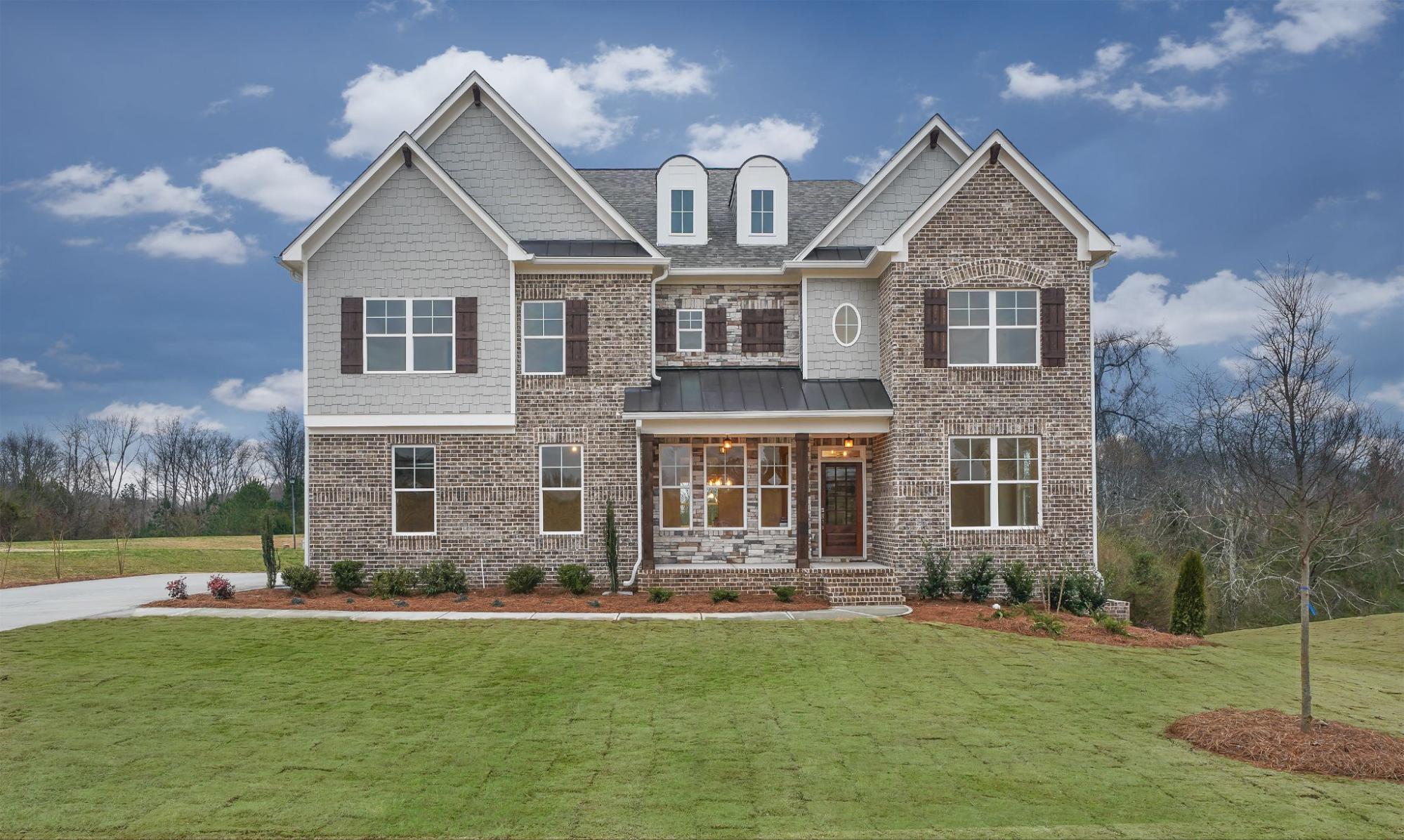  A luxurious two-story brick and stone custom home with a green lawn at Traditions of Braselton. 