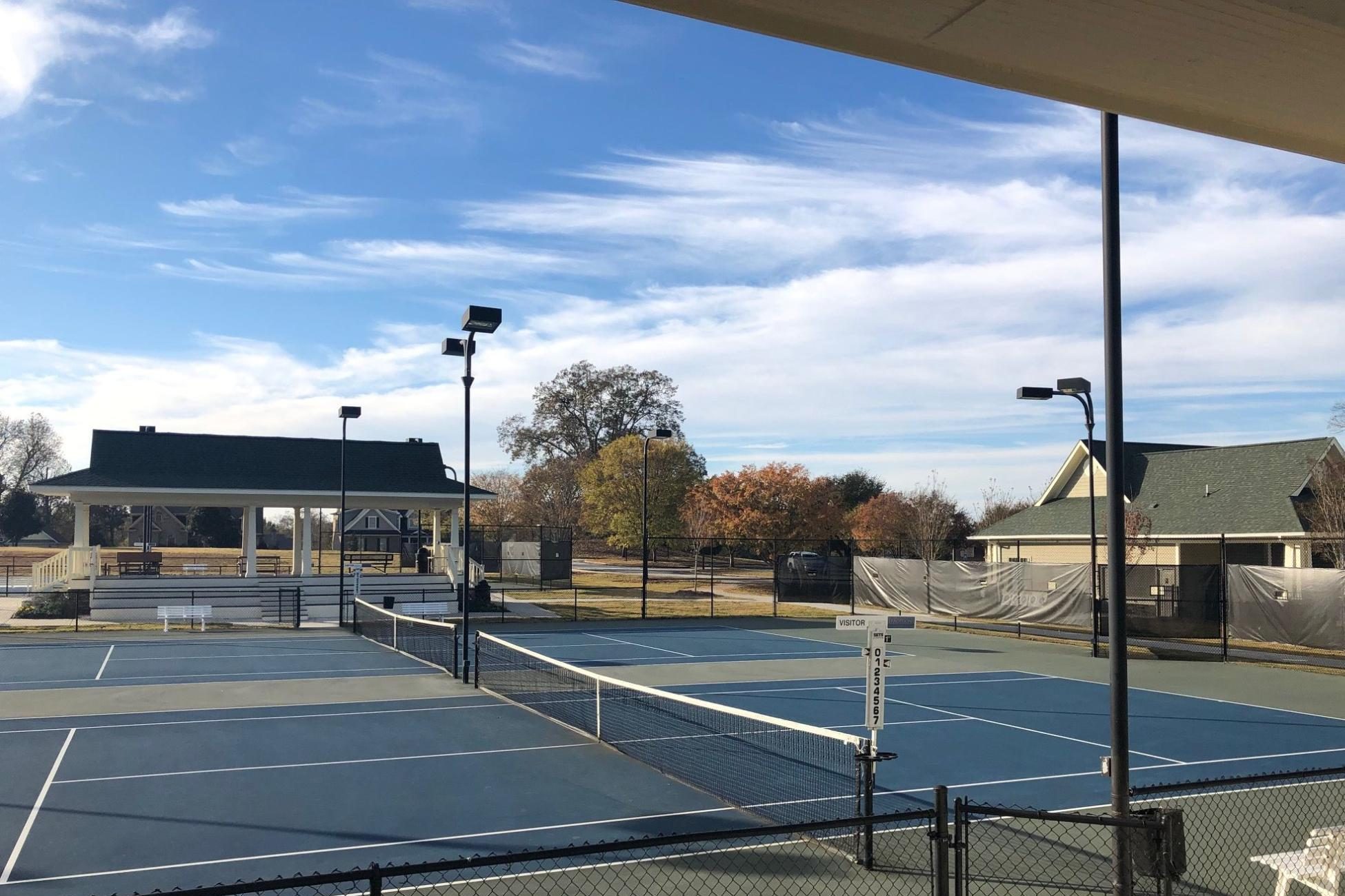 Multiple outdoor blue tennis and pickleball courts with stadium spectator seating.