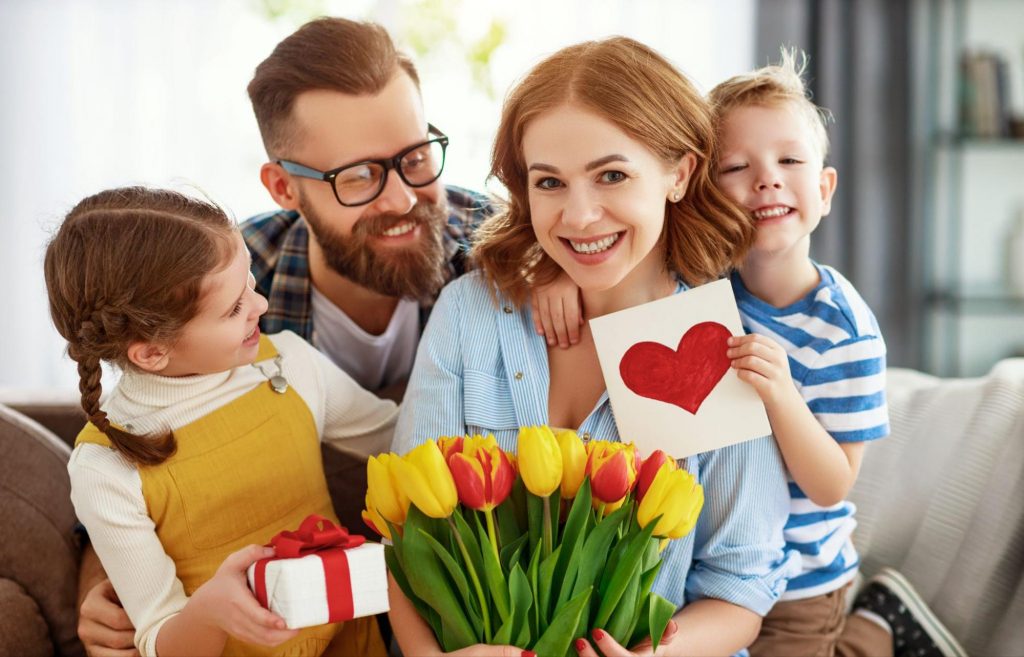 Happy family portrait with mother holding yellow tulips and kids presenting gifts for Mother's Day. ©Evgeny Atamanenko
