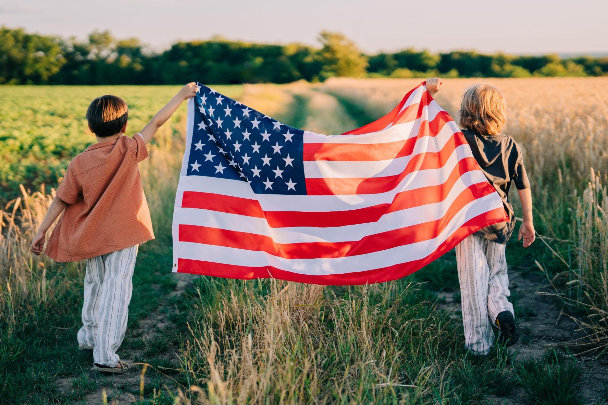 Two young children running through a grassy field while holding a large American flag open between them.
©Stock Holm