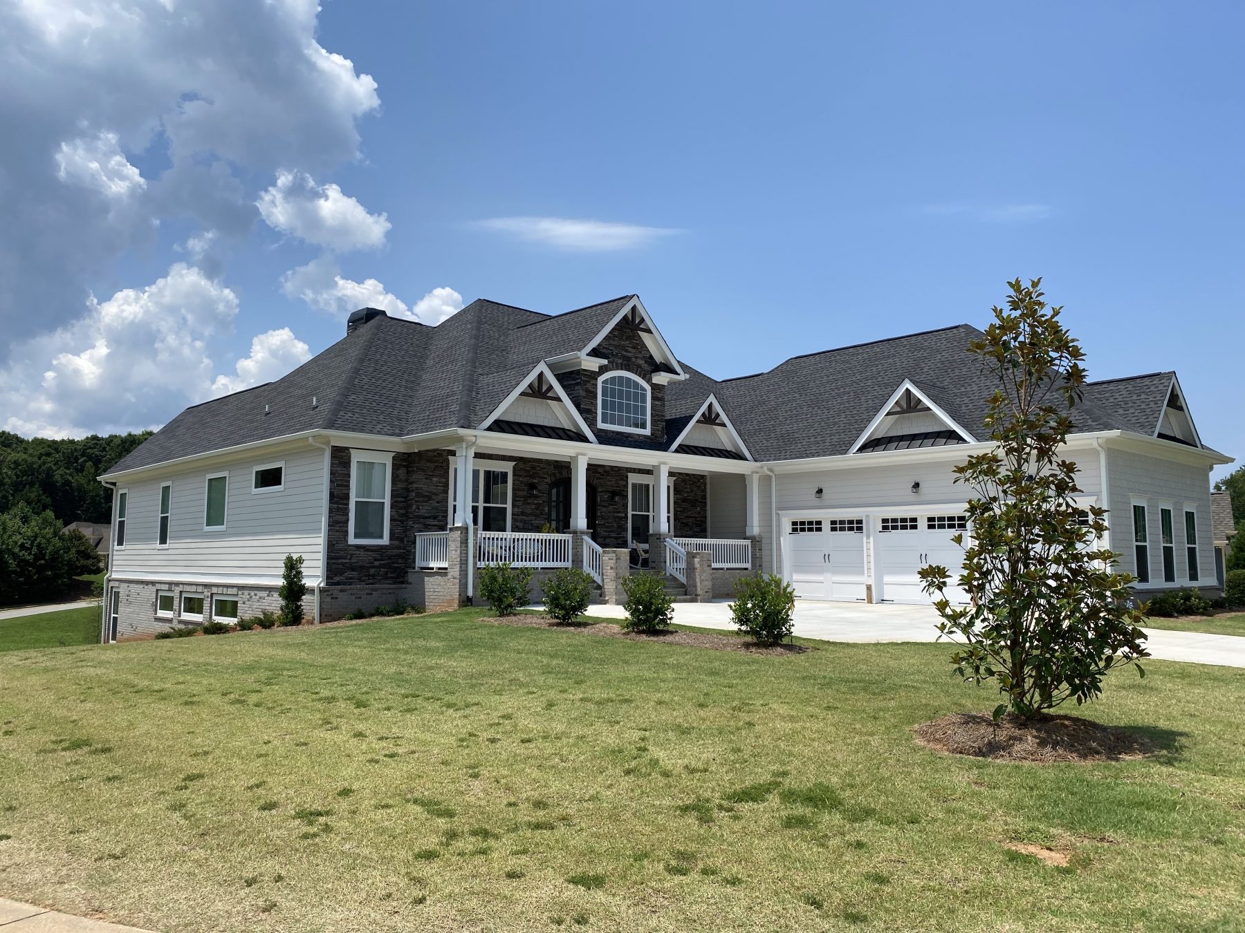 A spacious, modern farmhouse-style two-story new construction home featuring a stone facade, wrap-around front porch, and manicured green lawn.