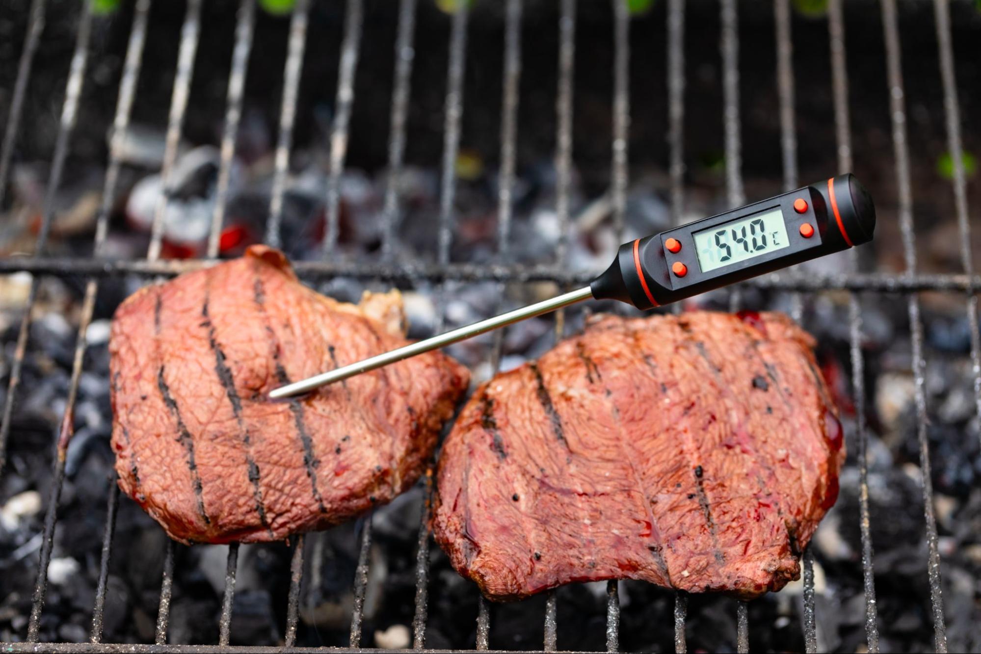 Digital meat thermometer checking steaks grilling on an outdoor backyard barbecue. ©Dmitry Naumov