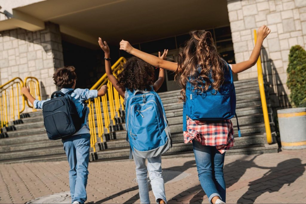 Happy students wearing backpacks walking up school steps on the first day of school. ©Inside Creative House