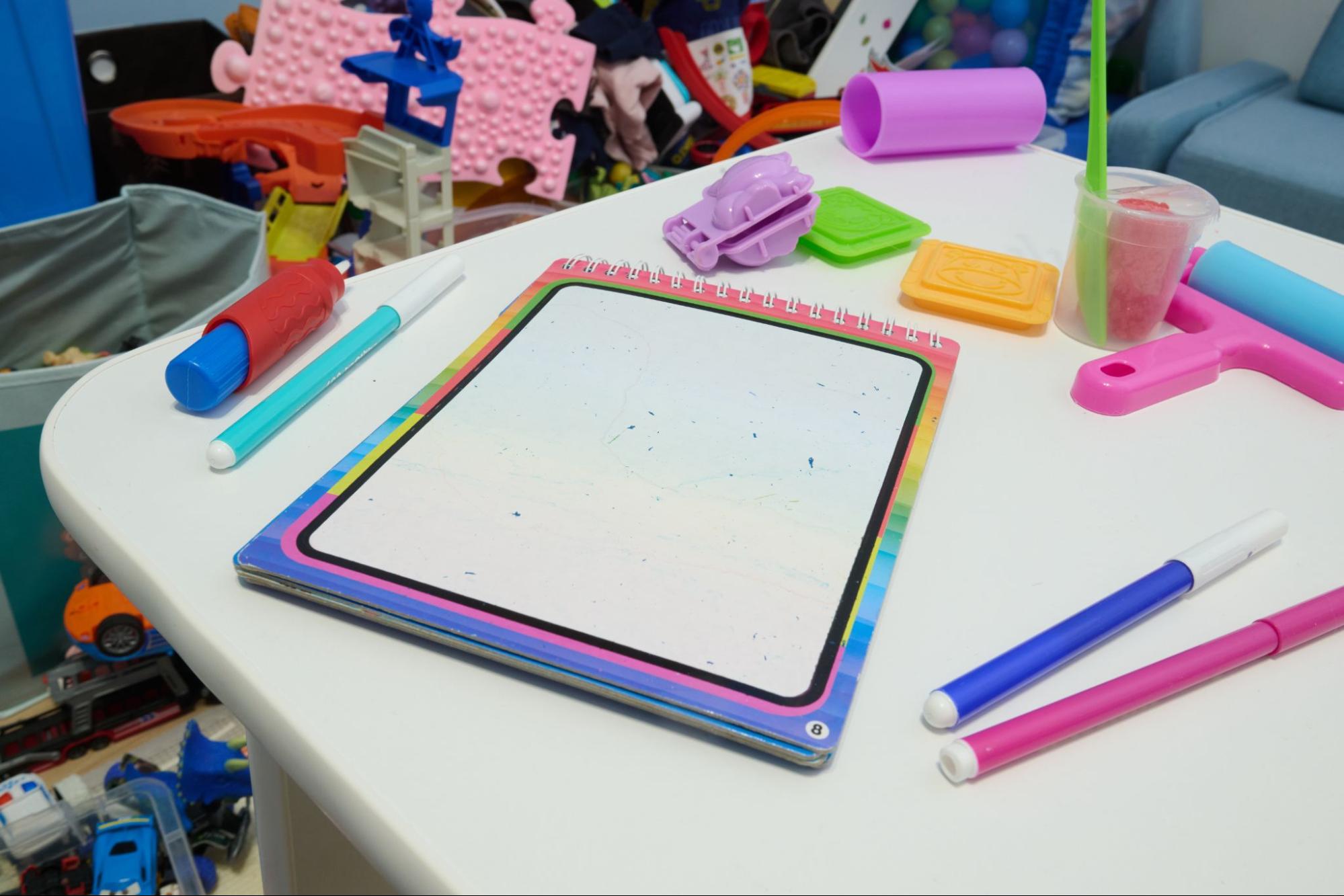 Reusable dry-erase notebook with colorful markers on a kid's homework desk. ©Elizaveta Korotkova
